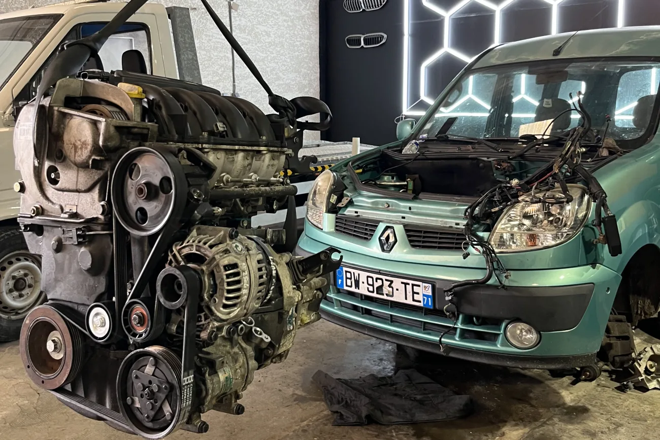 Moteur déposé à la grue d'atelier à côté d'un Renault Kangoo en réparation chez ISLK